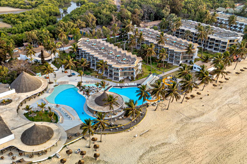 Hotel z basenami, palmami i plażą widziany z lotu ptaka.