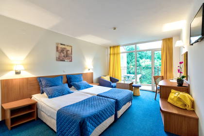 Pokój hotelowy z dwoma łóżkami, balkonem i żółtymi dodatkami.