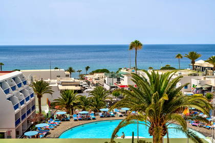 Hotel z basenem, morze i palmy w tle.