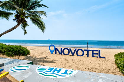 Napis "NOVOTEL" na plaży. W tle palma i ocean.