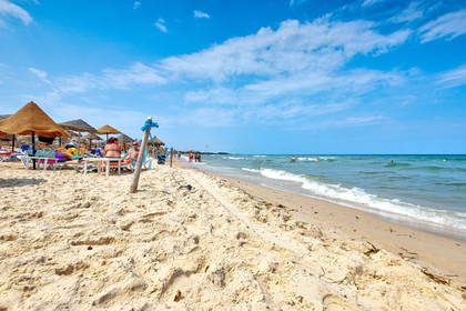 Plaża z parasolami i leżakami w słoneczny dzień.