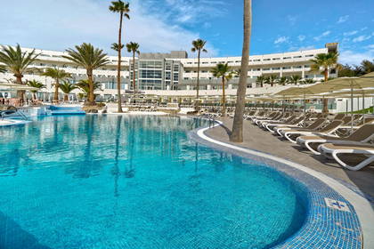 Hotelowy basen z leżakami i palmami w tle.