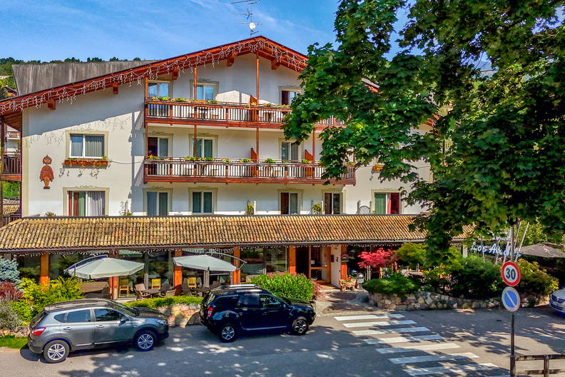 Trzypiętrowy budynek z terakotowymi balkonami i zaparkowanymi samochodami.