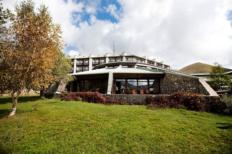 Hotel z kamienia i szkła otoczony zielenią.