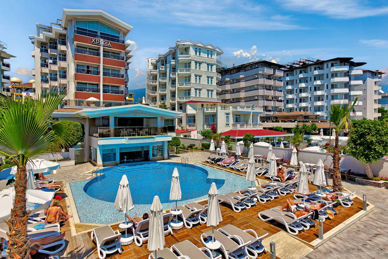 Basen z leżakami otoczony budynkami hotelowymi w słoneczny dzień.