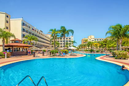Kompleks hotelowy z basenem, leżakami i palmami.