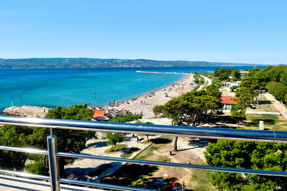 Widok z balkonu na plażę z turkusową wodą i zieloną roślinnością.
