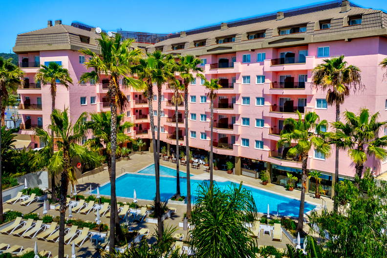 Różowy hotel z basenem otoczony palmami.