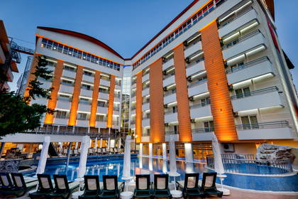 Nocny widok na hotel z basenem i leżakami.