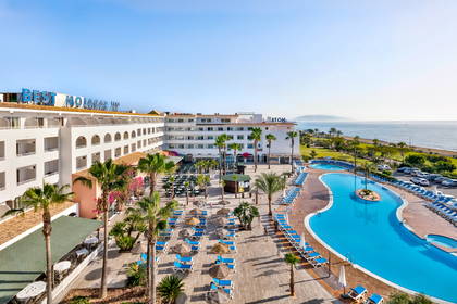 Hotel z basenem, leżakami i palmami widziany z góry.