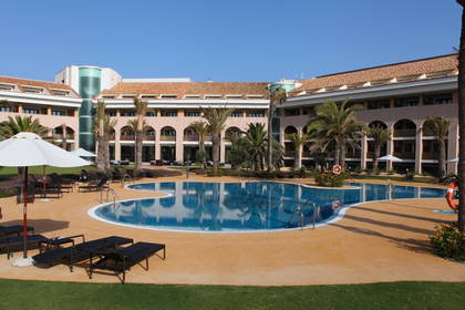 Kompleks hotelowy z basenem, leżakami i palmami.