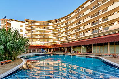 Zakrzywiony hotel z balkonami odbija się w tafli basenu.
