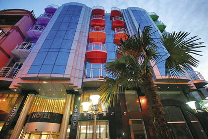 Fasada hotelu z kolorowymi balkonami i palmą.