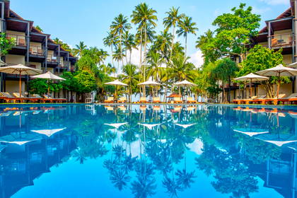 Basen w tropikalnym kurorcie otoczony palmami i budynkami.