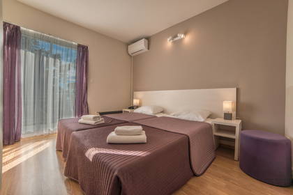 Pokój hotelowy z dwoma łóżkami, stolikiem nocnym i fioletowymi dodatkami.