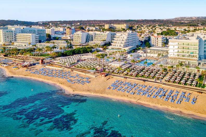 Plaża z leżakami i parasolami widziana z góry. W tle hotele.