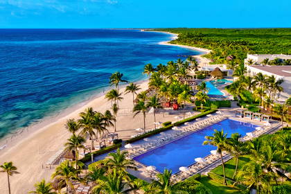 Resort z basenami, palmami i plażą widziany z góry.