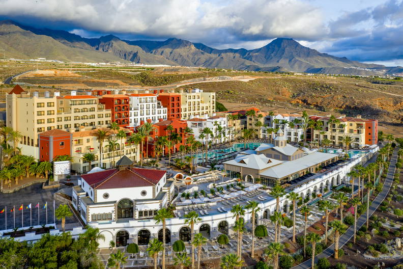 Kompleks hotelowy z basenami i palmami w otoczeniu gór.