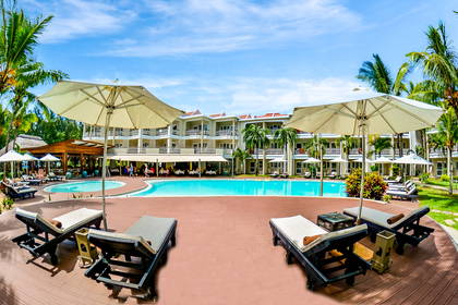 Resort z basenem, leżakami i palmami w słoneczny dzień.