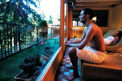 Wnętrze spa. Mężczyzna w ręczniku siedzi, a kobieta leży na leżance.