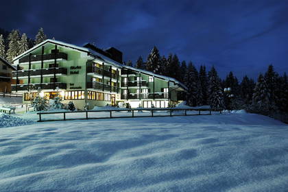Oświetlony hotel "Alaska" w zimowej scenerii. Wokół śnieg i drzewa.