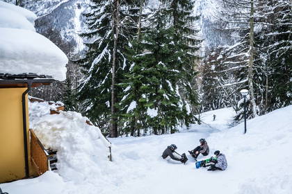 Trzy osoby siedzą na śniegu obok snowboardu w zimowym krajobrazie.