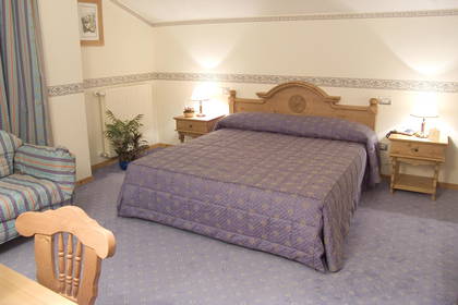 Pokój hotelowy z łóżkiem, stolikami nocnymi i fotelem.