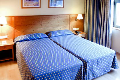 Pokój hotelowy z dwoma łóżkami, lampkami i zasłonami.