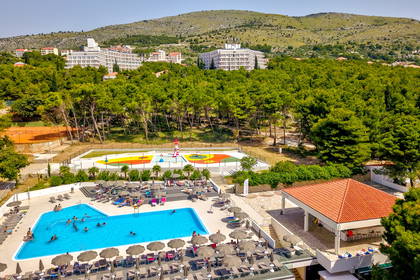 Basen hotelowy z leżakami i parasolami, widok z góry. W tle budynki.