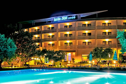 Oświetlony hotel z basenem nocą.