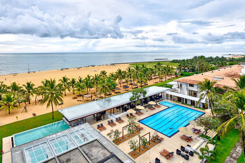 Hotel z basenami i plażą z palmami, widok z góry.