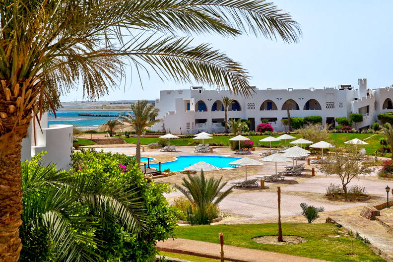 Basen, palmy i biały budynek hotelu.