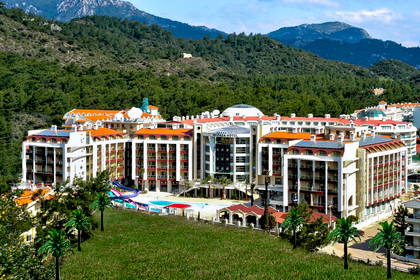 Hotel z basenem na pierwszym planie i zalesione wzgórza w tle.