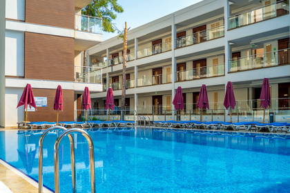 Hotelowy basen z błękitną wodą i leżakami, na tle budynku z balkonami.