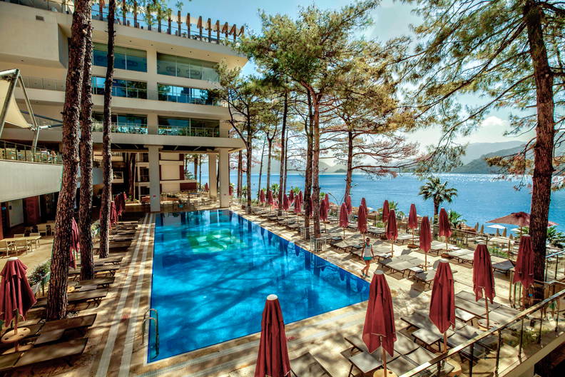 Hotelowy basen z leżakami nad morzem, w otoczeniu sosen.