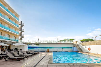 Basen hotelowy z rzędem leżaków pod parasolami. W tle hotel i błękitne niebo.