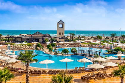 Hotelowy basen z leżakami i parasolami. W tle ocean i wieża.