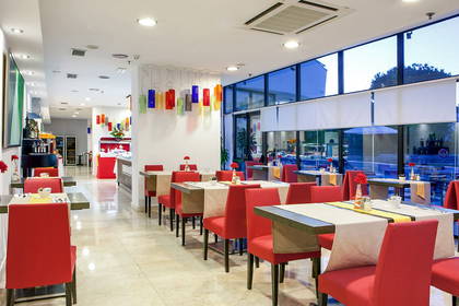 Restauracja z czerwonymi krzesłami i dużymi oknami.