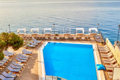Basen hotelowy z leżakami i widokiem na morze, zdjęcie z góry.