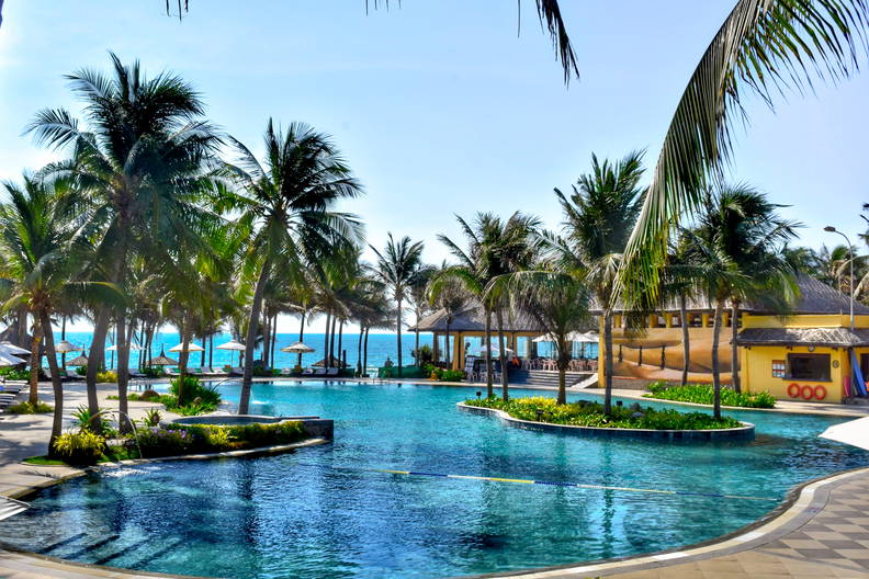 Kompleks basenowy z palmami i budynkiem w tle.