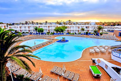 Kompleks hotelowy z basenem, leżakami i palmami, widok z góry.
