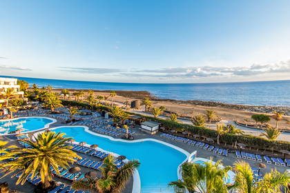 Hotel z basenami i plażą w słoneczny dzień.