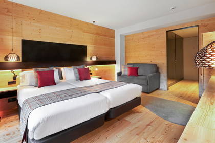 Pokój hotelowy z dwoma łóżkami, drewnianymi panelami na ścianach i szarą kanapą.
