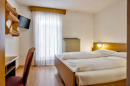 Pokój hotelowy z łóżkiem, biurkiem i telewizorem. W pokoju znajduje się okno.