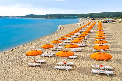 Plaża z pomarańczowymi parasolami i leżakami, widok z góry.