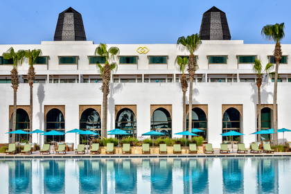 Hotel z basenem, palmami i leżakami.