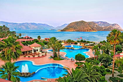 Hotel z basenami i palmami, w tle morze.