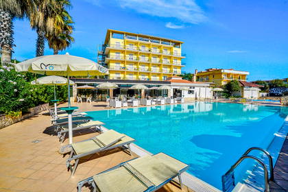 Hotel z basenem i leżakami w słoneczny dzień.