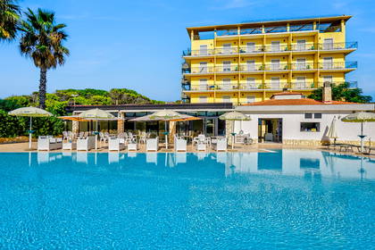 Basen przy hotelu w kolorze żółtym, otoczony palmami i parasolami.