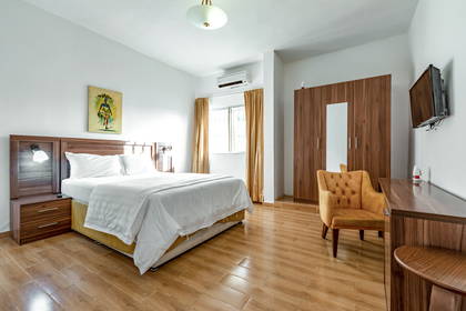 Jasny pokój hotelowy z łóżkiem, szafą, fotelem i telewizorem.